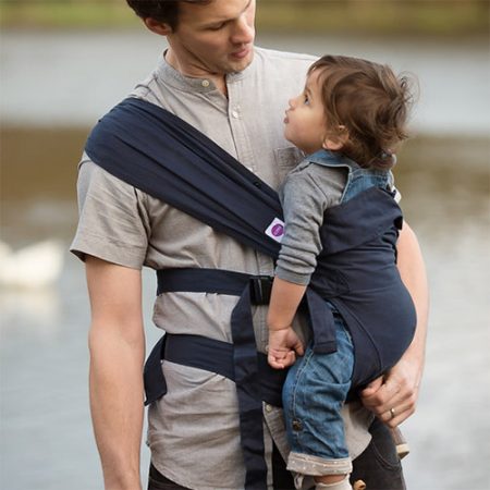 Man carries older baby on his hip in midnight blue Izmi baby carrier