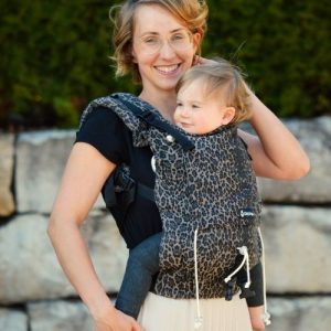 Smiling woman carries baby facing towards her in Didymos DidySnap baby carrier in Leo