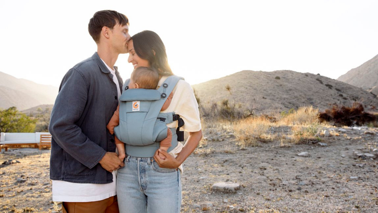 Woman carries baby in Ergobaby Omni Dream baby carrier while man kisses her head
