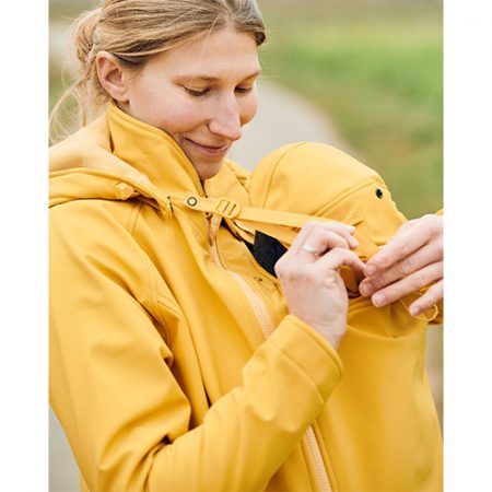 Woman carrying baby on her front while wearing the Mamalila Allrounder Softshell Babywearing Jacket in Mustard