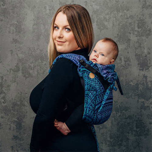 Woman carries baby on her back in Lenny Lamb Onbuhimo baby carrier in Peacock's Tail Provance fabric, side view