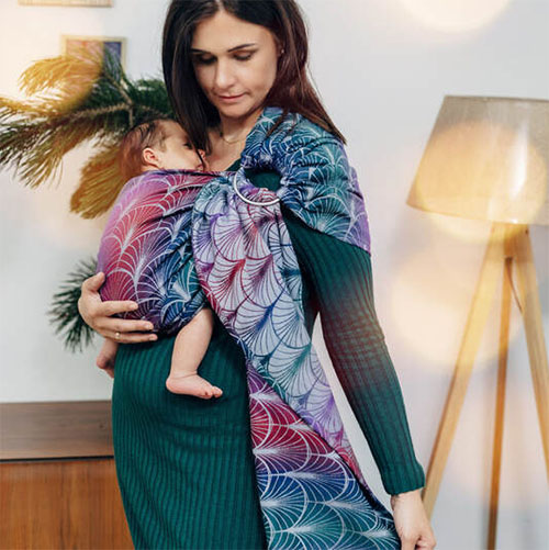 Woman carries baby on her front in Lenny Lamb Ring Sling in Deco Kingdom fabric