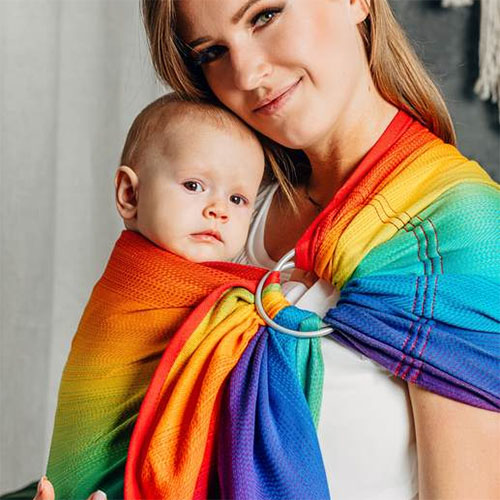 Woman carries baby on her front in Lenny Lamb Ring Sling in Rainbow Baby fabric