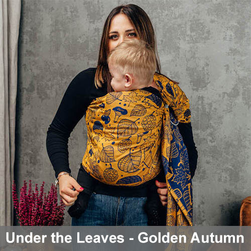 Woman carries baby on her front in Lenny Lamb Ring Sling in Under the Leaves Golden Autumn fabric