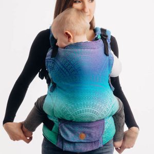 Woman carries baby facing towards her in Lenny Lamb LennyUpgrade Baby Carrier in blue Peacock's Tail Fantasy fabric