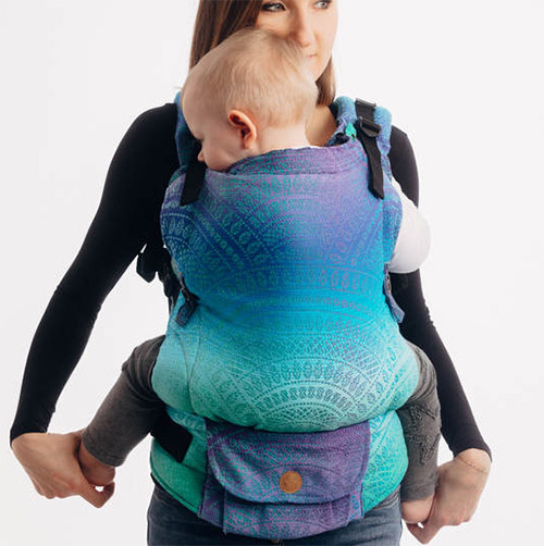 Woman carries baby facing towards her in Lenny Lamb LennyUpgrade Baby Carrier in blue Peacock's Tail Fantasy fabric