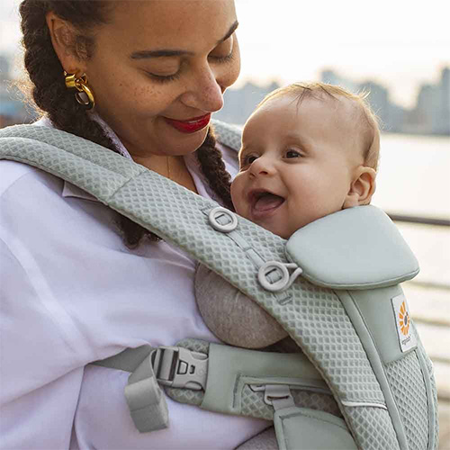 Woman carries baby facing towards her in Sage Green Ergobaby Omni Breeze carrier, close up
