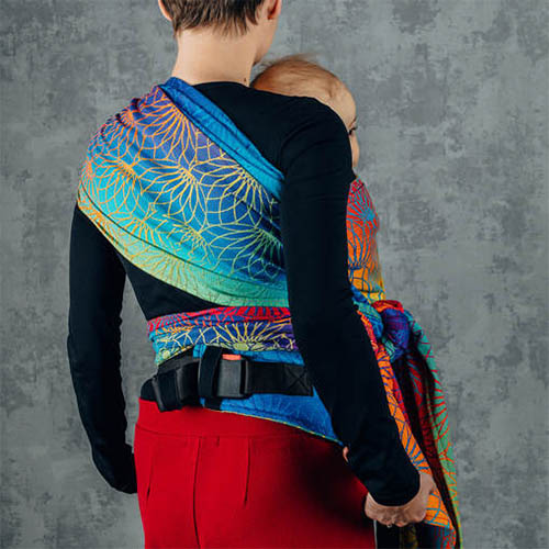 Woman carrying baby on her front in Lenny Lamb Lenny Hybrid Half Buckle Baby Carrier in Rainbow Lotus