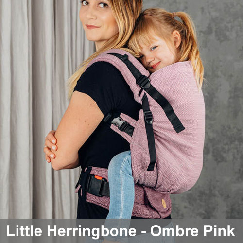 Woman carries toddler on her back in Lenny Lamb Preschool carrier in Little Herringbone fabric in Ombre Pink