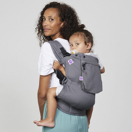 Woman carries toddler on her back in Izmi Toddler Carrier with Zip Hood
