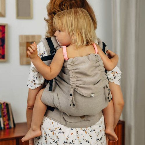 Woman carries toddler on her back in Lenny Lamb Preschool carrier in beige Peanut Butter colourway